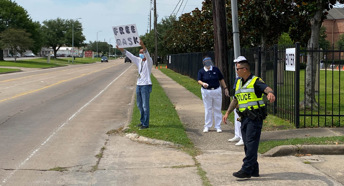 志工頂著烈日，在路邊舉著牌子，上面寫著「免費口罩 Free Masks」，希望有需要的人能夠繼續獲得物資來防疫。攝影／劉本琦