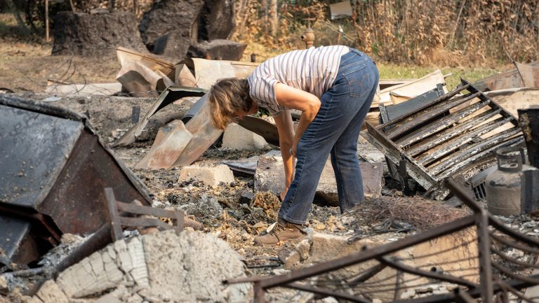 罗嫔·古德温（Robyn Goodwin）走到废墟家园中，搜索未被大火烧成灰烬的物品。摄影 / 曾奂珣