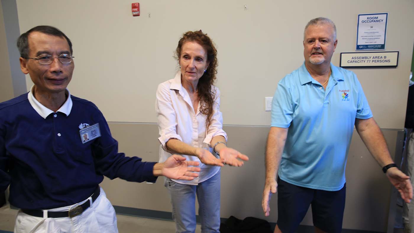 Zhenxiong Luo, Tzu Chi USA Southern Region Executive Director (left), teaches Collier County Commissioner Penny Taylor (middle) and Jim Ludwig, Executive Director of the non-profit Pickleball For All, some sign language gestures.