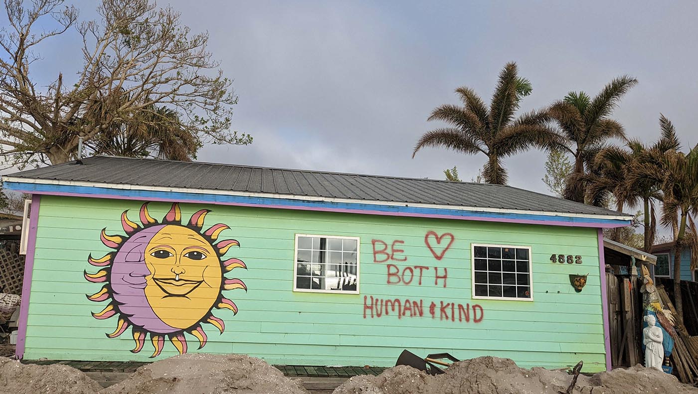 house with a message scrawled on its side: “Be Both Human & Kind.”