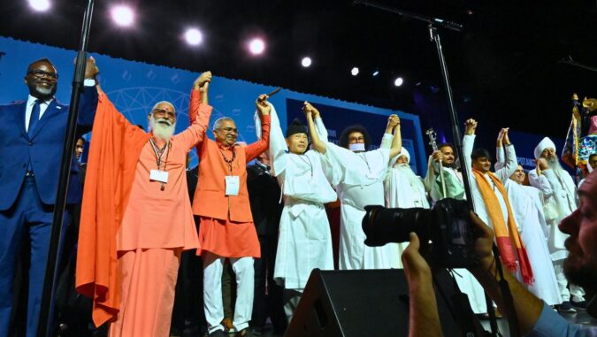 people from around the world join hands at the 2023 convening of the Parliament of the World’s Religions