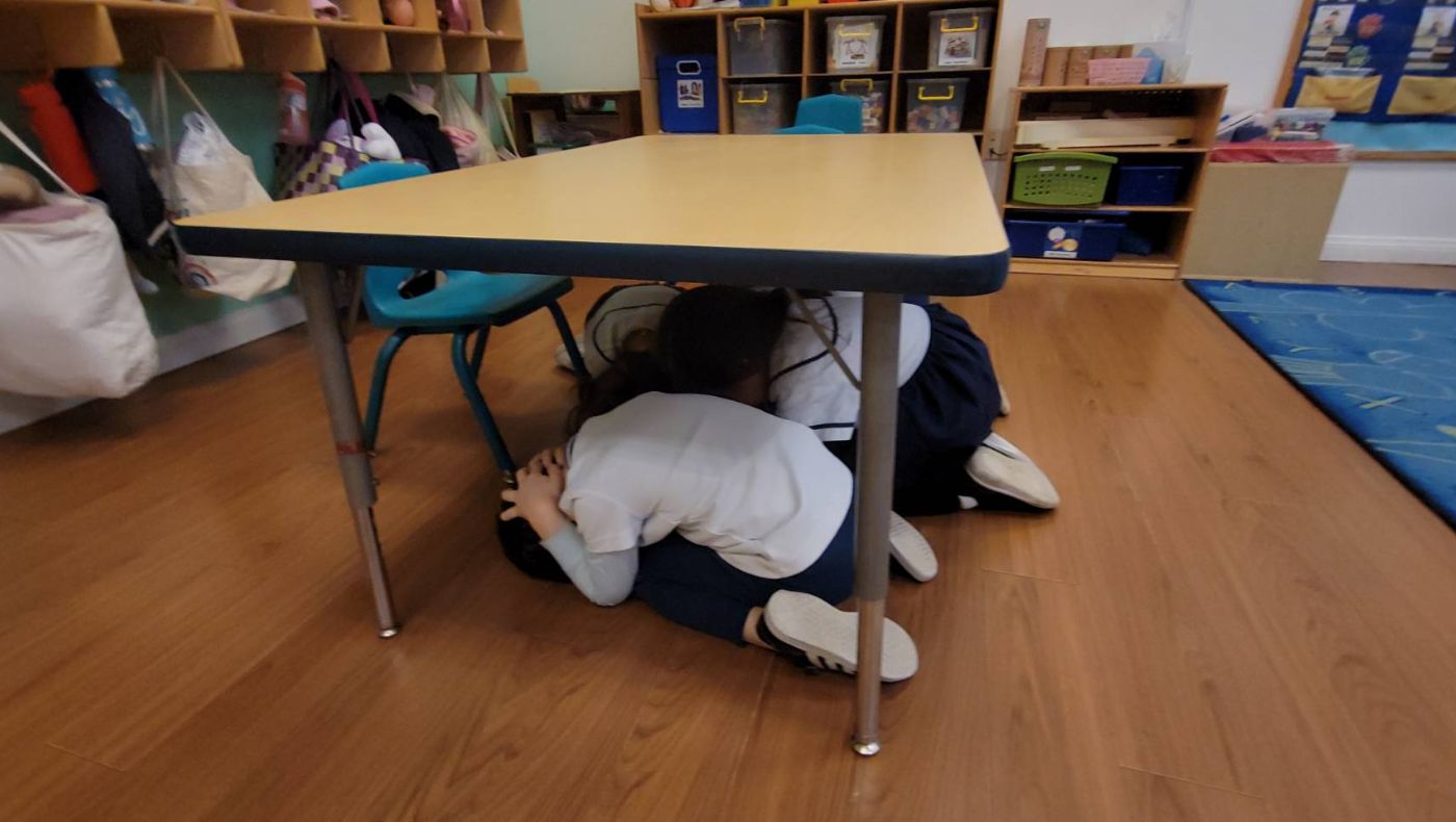 The children quickly hid under the table, holding their heads with their hands, practicing key shock-absorbing skills such as "get down", "cover" and "hold steady/stay still".