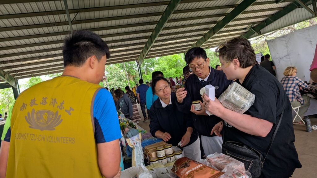 志工蔡宜靜與溫倉彬熱情向會眾阿曼達·貝爾（Amanda Bell）說明各種淨斯產品，她被志工的誠情感染，而願意購買嘗試，歡喜請購了六種不同的產品。攝影／陳宗坤