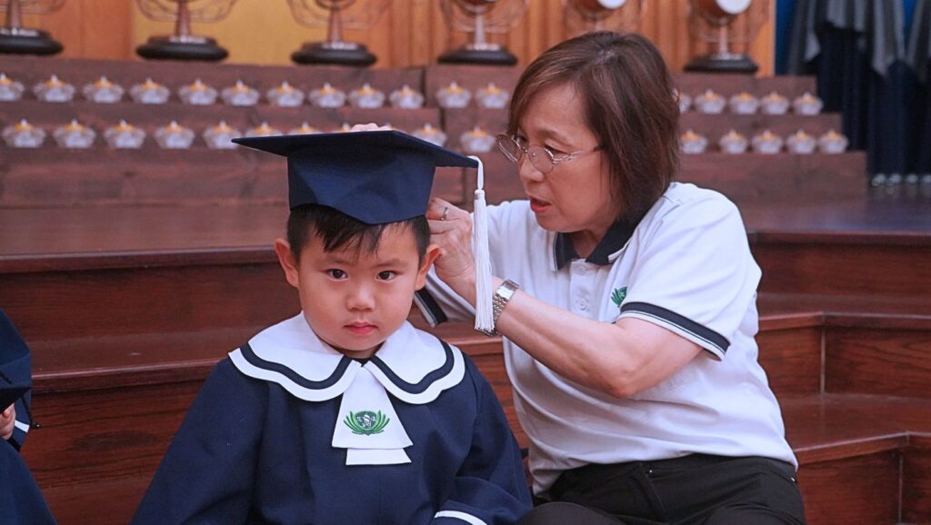 休士頓慈濟大愛幼兒園老師陳美玲(右)為畢業生多利安·鄭(左)整理方帽,迎接他人生中的第一個畢業典禮。攝影/葉晉宏