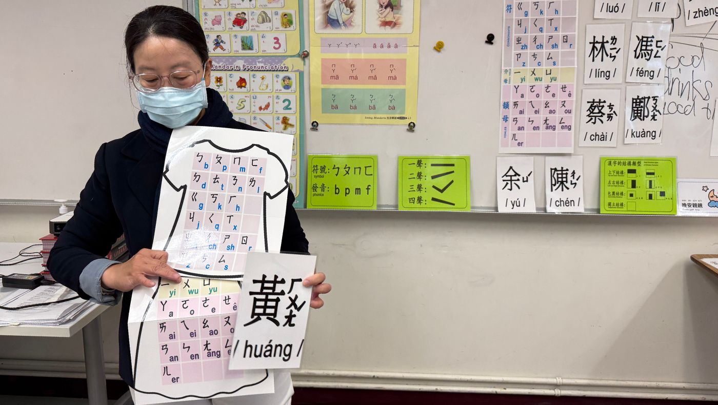 A teacher explains Chinese pronunciation during class, holding a character card and a phonetic chart. Photo/Lulu Yin