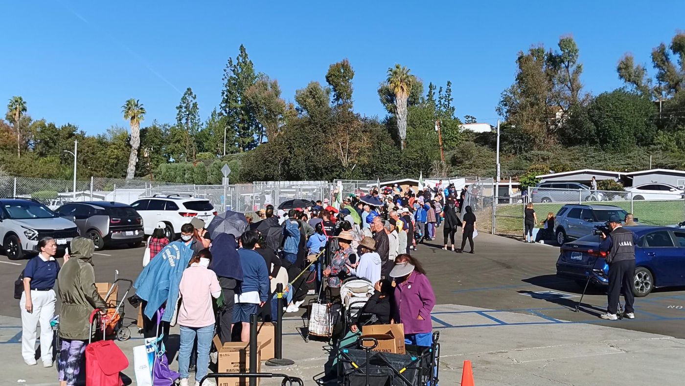 Long lines formed early in the morning at the distribution site, with people pulling trolleys or carrying bags, or bringing their children to collect the supplies. (Photo by Chen Xiuwen)