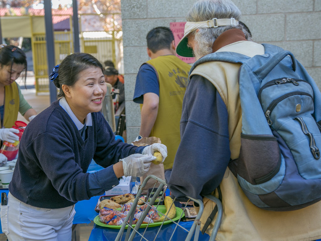 Volunteer smiles while handing food to a man at a charity distribution.