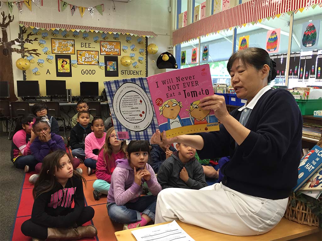 Woman reading the book "I Will Never Not Ever Eat a Tomato" to a group of seated children.