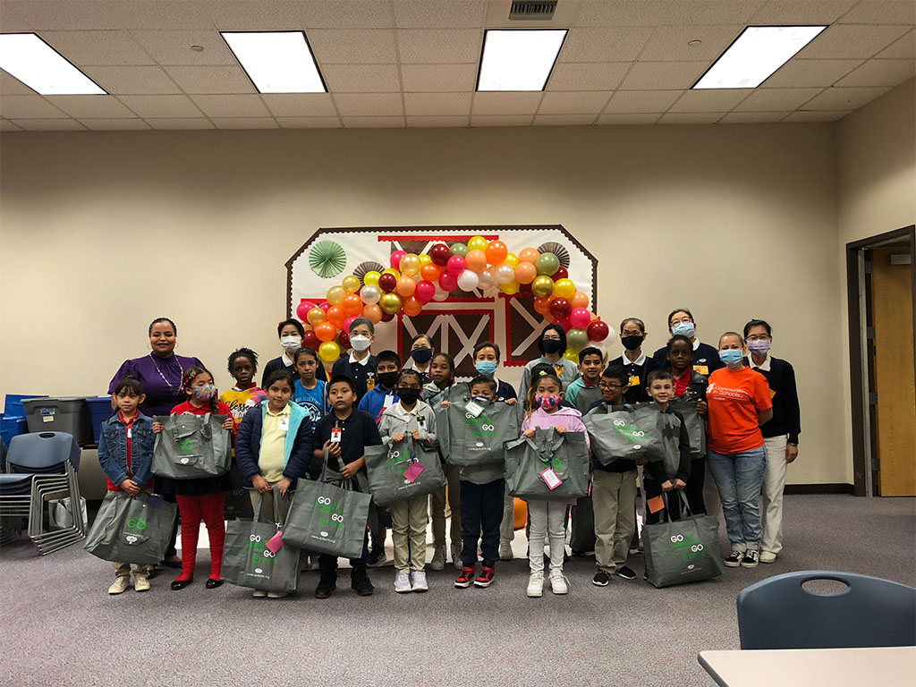 Group photo of students holding gift bags with teachers and volunteers.