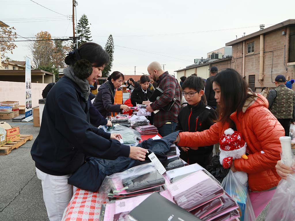 Volunteers handing clothing and supplies to a mother and son outdoors.