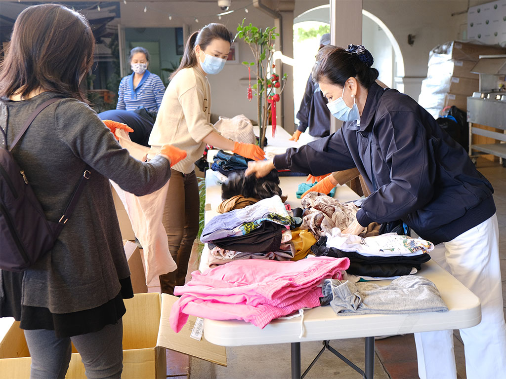 olunteers organize stacks of donated clothes on tables indoors.