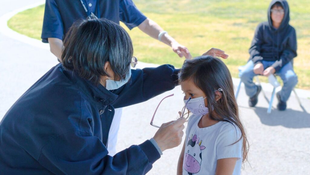 Volunteer helping little girl to wear her glasses
