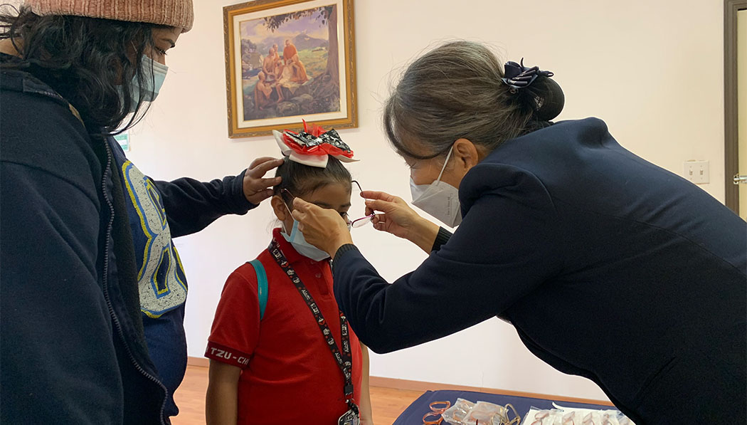 志工在「慈濟墨西哥提娃那園區」為接受眼科義診的學童戴上新配的免費眼鏡。圖片來源／李靜誼