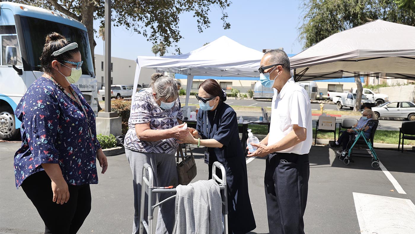 At a Tzu Chi Mobile Clinic outreach, then Board Chairman at the Buddhist Tzu Chi Medical Foundation, Dr. William Keh (right), and his wife, veteran Tzu Chi volunteer Mary Keh (second right), give pandemic-related personal protection supplies to those who come for medical care.