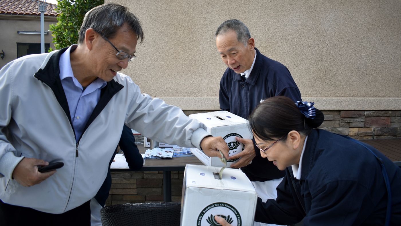 In 2018, wildfires broke out in California, USA. Tzu Chi volunteers in Los Angeles went to supermarkets to raise funds for charity on November 18. William Keh (back right) and Mary Keh (front right) hold donation boxes, and people donate money.
