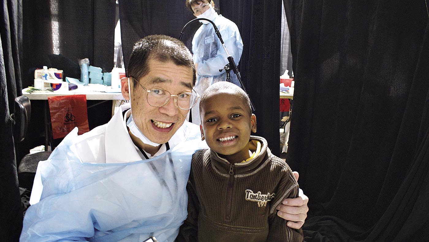 2007年卡崔娜義診牙醫師陳建全完成牙科診療後，攬著一名原本害怕補牙的孩童，兩人開心露齒而笑。攝影／王惠平