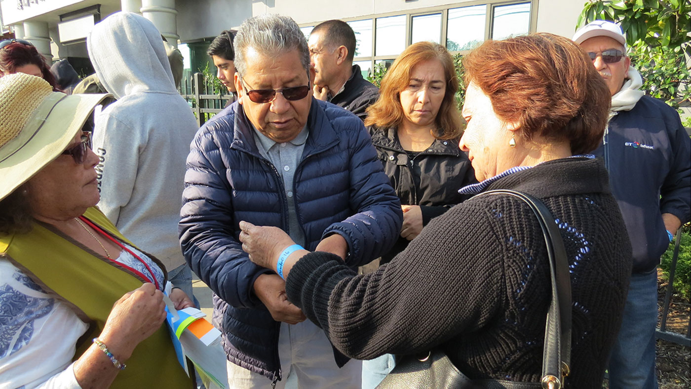Hispanic Tzu Chi volunteers attach name tags on the wrists of people lining up for medical outreach at the Tzu Chi Wilmington Community Clinic. Photo/Emerald Hsu