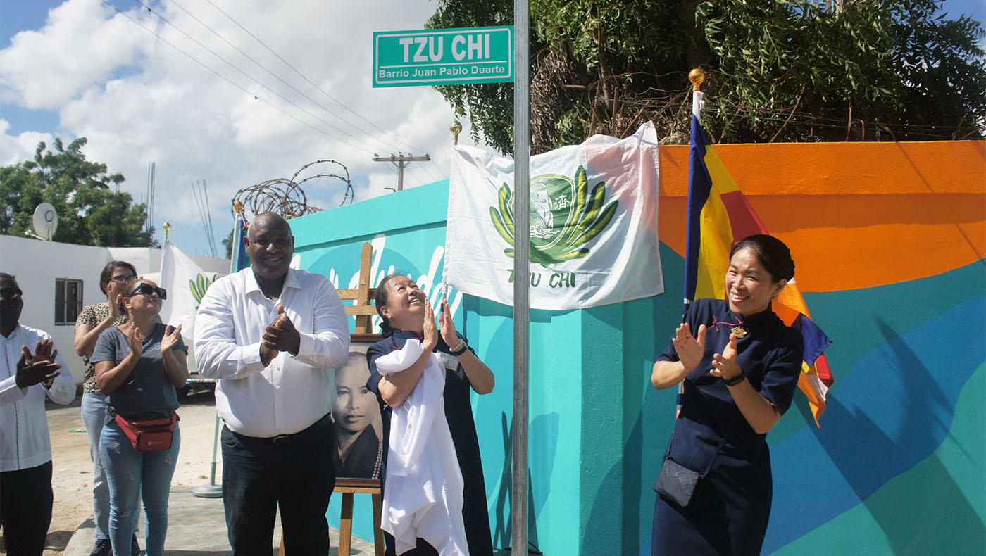 Debby, Tzu chi volunteer and La Romana locals clapping hands in front of Tzu chi flag and road sign