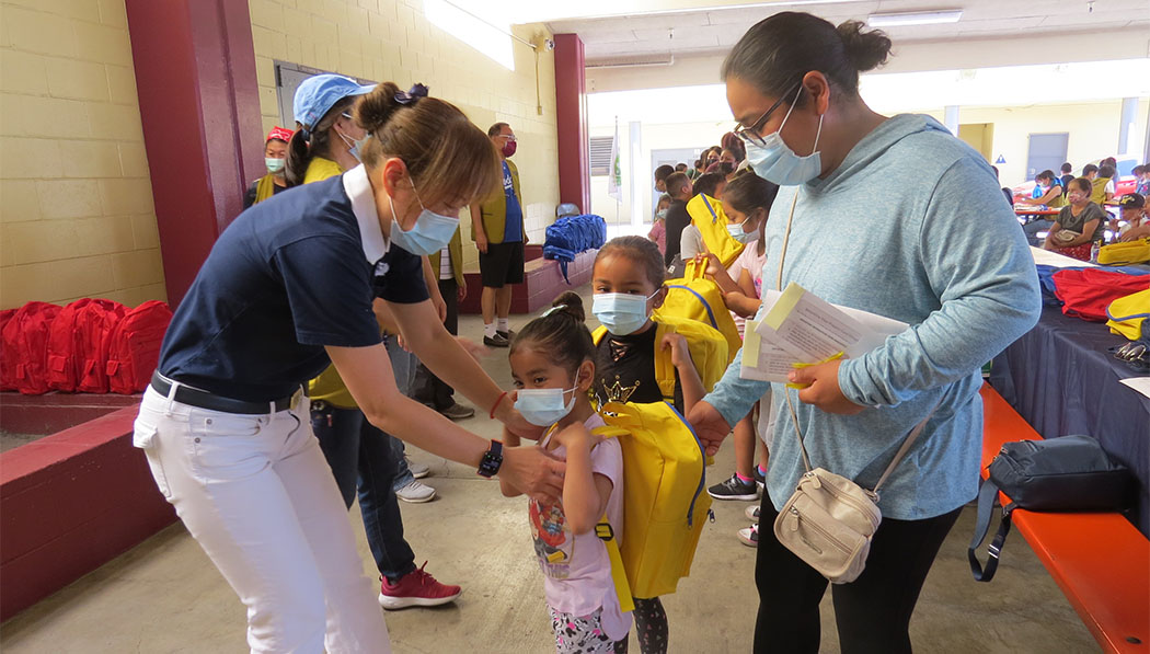 In August 2022, with the resumption of in-person learning, Cerritos Service Center volunteers provide schoolchildren with supply-filled backpacks, including PPE, at Miles Avenue Elementary in Huntington Park, California.