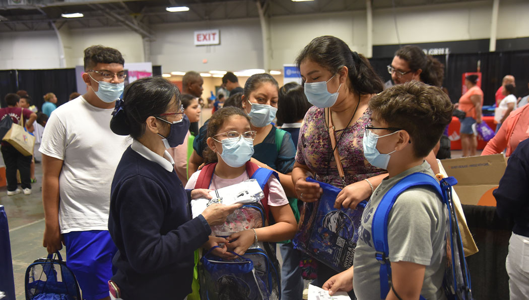 A Tzu Chi volunteer chats with a family about what they’ll receive with their school uniform, including PPE, at the Dallas Mayor’s Back to School Fair.