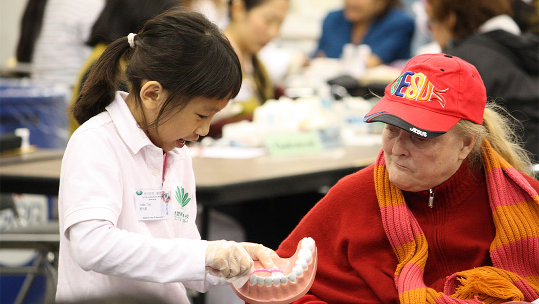 A student from Tzu Chi Academy, Houston, shows a care recipient how to brush her teeth